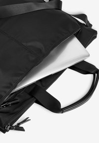 Czarna torba na laptopa wykonana z trwałego materiału, z zamknięciem na zamek błyskawiczny i regulowanymi paskami. Widać srebrny laptop częściowo widoczny w środku.