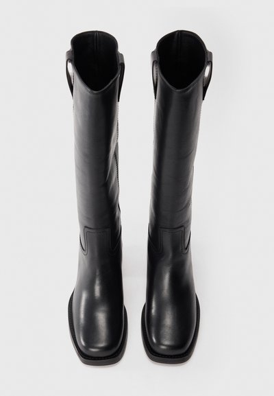 Black leather knee-high boots with a pointed toe, decorative stitching, and pull tabs at the top. Smooth texture and flat soles.