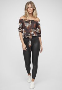 Blouse décolletée avec un imprimé de feuilles de palmier en noir, orange et blanc, associée à des leggings noirs brillants et des baskets blanches.