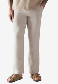 Pantaloni in lino beige chiaro con una texture liscia, design a gamba dritta e tasche laterali, abbinati a sandali verde oliva.
