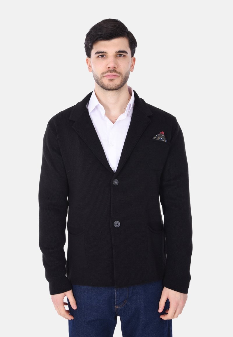 Cardigan nero lavorato a maglia con due tasche frontali, colletto a scialle e tre bottoni. Accentuato con un fazzoletto da taschino a motivi.