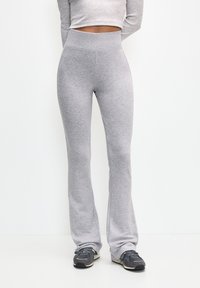 Pantalon de survêtement évasé gris en tissu doux, doté d'une taille haute et d'une texture lisse. Porté avec des chaussures de sport foncées.