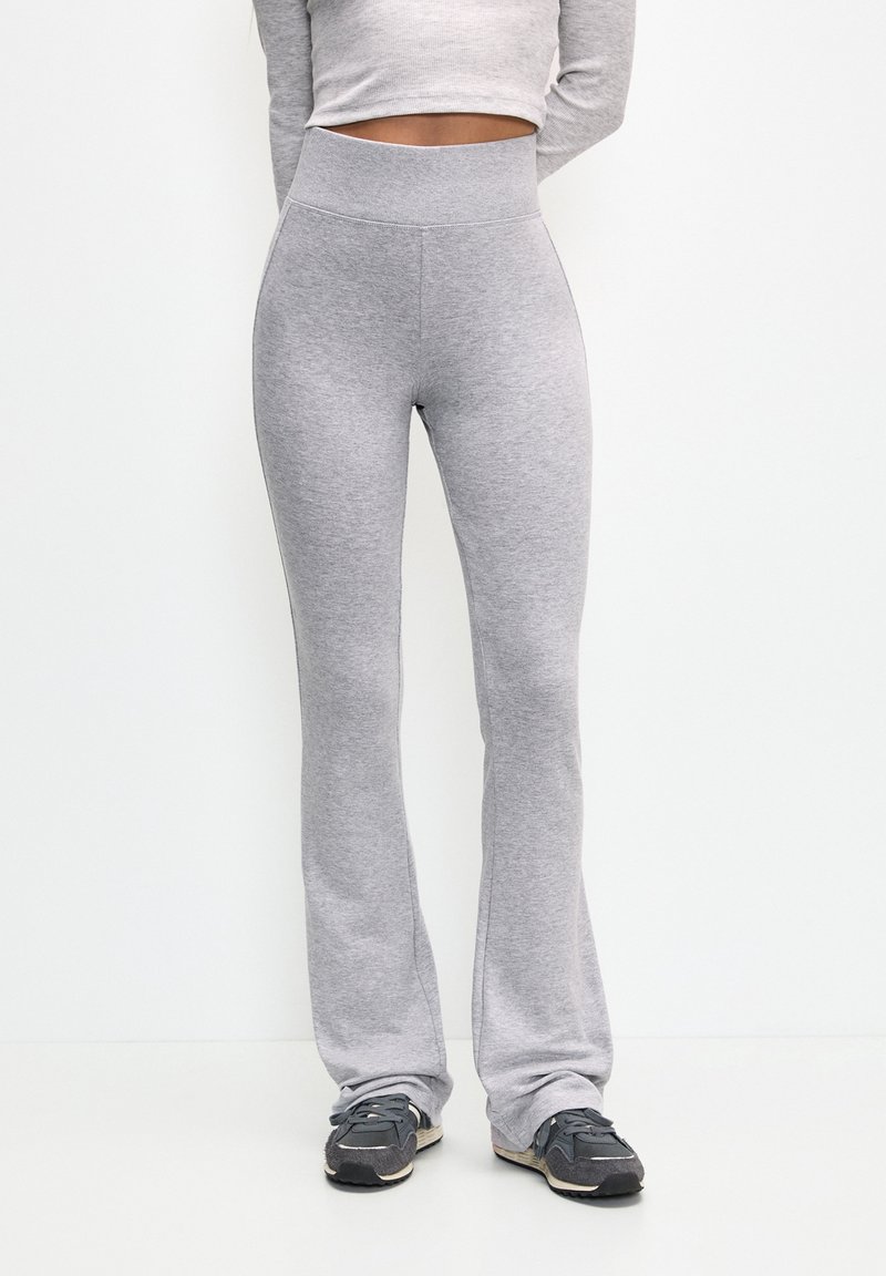 Pantalon de survêtement évasé gris en tissu doux, doté d'une taille haute et d'une texture lisse. Porté avec des chaussures de sport foncées.