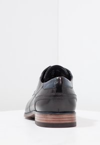 Chaussure Oxford en cuir noir avec une finition lisse, un bout arrondi et un talon empilé en bois. Présente des coutures discrètes et un accent de talon contrastant.