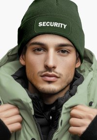Green ribbed beanie with "SECURITY" label; oversized padded jacket with a light green exterior and black inner lining; smooth skin texture.