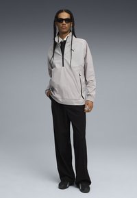 Chaqueta de pullover gris claro con media cremallera, panelado texturizado, bolsillo frontal y puños elásticos, combinada con pantalones de pierna ancha negros y zapatillas.