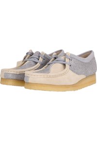 Chaussures en suède beige clair et gris avec une texture douce, semelles en caoutchouc plates et un design à lacets présentant des lacets gris et des détails cousus.