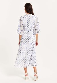 White dress with blue polka dots and floral print. Features short, flared sleeves and a cinched waist, falling to mid-calf length.