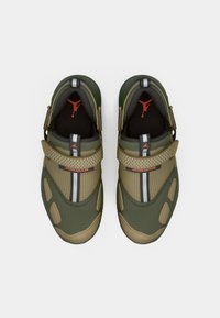 Ζευγάρι πράσινων και καφέ Jordan slip-on αθλητικών παπουτσιών με βέλκρο λουράκια και κόκκινα λογότυπα Jumpman σε μαύρες σόλες, εμφανιζόμενο από πάνω σε λευκό φόντο.