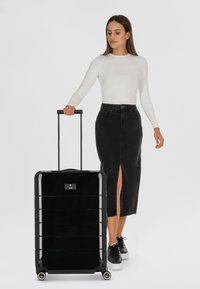 Black hard-shell suitcase with a glossy finish, featuring a retractable handle, four wheels, and a minimalistic logo on the front.