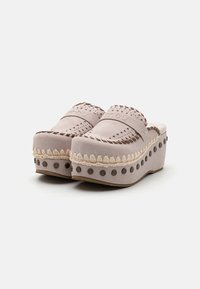 Sabots avec une tige en daim rose pastel, des accents tissés et une plateforme épaisse ornée d'agrafes en métal et de détails tressés.