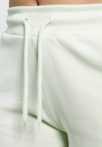 Ljusgröna sweatpants har en ribbad midja med dragsko och är tillverkade av ett mjukt, slätt material. Detaljer inkluderar en subtil lyster och en avslappnad passform.