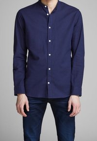 Camicia blu navy con bottoni e collo alla coreana, realizzata in un tessuto liscio, con bottoni bianchi e maniche lunghe.
