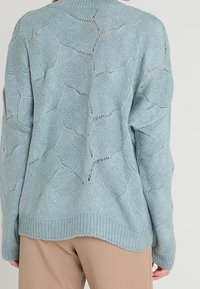 Jasnoniebieski sweter z dzianiny z teksturowanym wzorem liści, o luźnym kroju, z prążkowanym dołem i ażurowymi detalami na całej powierzchni.