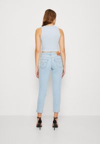 Light blue fitted jeans with a tapered design, featuring a high waist and distinctive back pocket stitching, paired with a fitted sleeveless top.