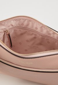 Růžová kožená taška s vnitřkem se zlatým zipem. Má hladkou texturu a nenápadné logo; uvnitř je podšitá vzorovanou látkou. Obsahuje malou kapsu.