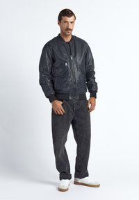 Svart läderbomberjacka med ribbade muddar, två framfickor och dragkedjestängning, matchad med mörka jeans och vita sneakers.