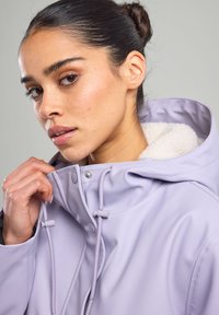 Lilac waterproof jacket with a fur-lined hood, adjustable drawstrings, and snap closures. Smooth texture, fitted design, and durable material.