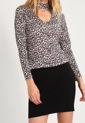 Woman wearing a long-sleeve leopard print top with a choker neckline and a fitted black mini skirt.