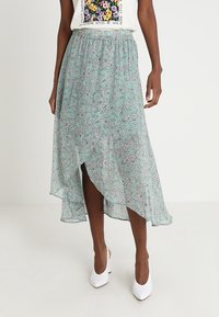 Lichtgewicht, mintgroene rok met een bloemmotief, een asymmetrische zoom en een elastische tailleband. Gedragen met een witte top en hakken.