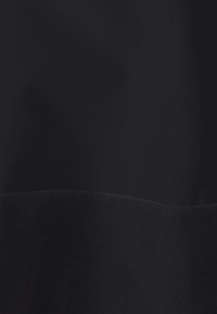 Schwarzer Stoff mit einer horizontalen Naht, die zwei unterschiedlich strukturierte Abschnitte aus glattem und geripptem Material trennt.