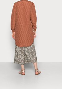 Vatteret lang jakke i rusten orange med ribbede manchetter, parret med blomsterprintede culottes og remmede metalliske sandaler.