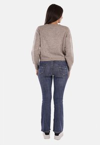 Maglione beige lavorato a maglia con scollatura rotonda, maniche lunghe e sottili decorazioni, abbinato a jeans a vita alta blu a zampa d'elefante e scarpe da ginnastica bianche.