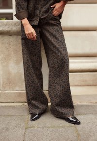 Pantalons larges à imprimé léopard en marron foncé avec un motif noir, associés à des talons aiguilles vernis noirs. Tissu lisse avec une coupe décontractée.