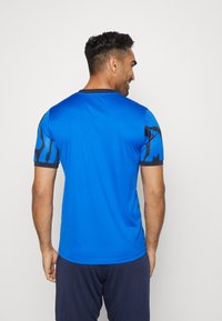Blaues Sportshirt mit kurzen Ärmeln, das mit schwarzen abstrakten Mustern verziert ist. Glattes, leichtes Material und ein Rundhalsausschnitt.