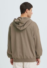 Sweat-shirt vert olive avec capuche, doté d'une coupe décontractée, de poignets et d'un ourlet côtelés, et d'une texture lisse. Coutures apparentes en accent sur les épaules.
