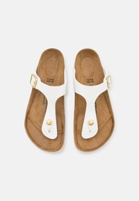 Witte flip-flopsandalen met een kurken voetbed, dunne banden, een goudkleurige gesp en een decoratieve knop bij de teenstuk.
