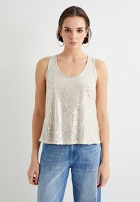 Ærmeløs beige tank top med pailletdetaljer. Løs pasform, rund halsudskæring, og nederste kant falder lige under taljen. Båret med blå jeans.