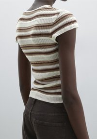 Knitted short-sleeve top in cream and brown stripes, featuring a fitted design and textured ribbed pattern. Paired with dark high-waisted jeans.