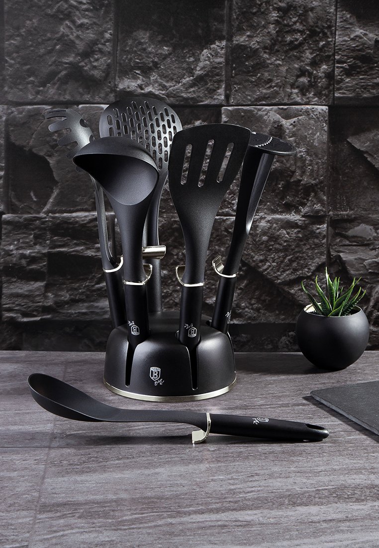 Zestaw czarnych utensyliów kuchennych w stojaku, w tym łyżka dziurkowana, łopatka i chochla. Eleganckie, matowe wykończenie z srebrnymi akcentami.