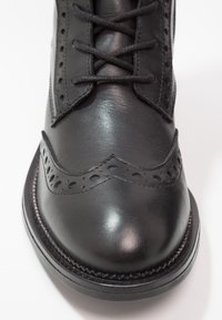 Scarpa in pelle nera con dettagli brogue, punta rotonda e design con lacci. Texture liscia con accenti cuciti lungo la suola.