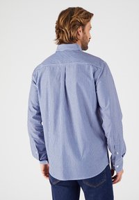 Camisa de botones a rayas en azul y blanco, con mangas largas, cuello y un sutil pliegue en la parte trasera. El material parece suave y ligero.