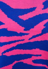 Πλεκτό ύφασμα με αφηρημένο σκισμένο μοτίβο σε φωτεινές ροζ και μπλε αποχρώσεις, που παρουσιάζει κοντινή υφή και λεπτομέρειες πλεγμένων νημάτων.