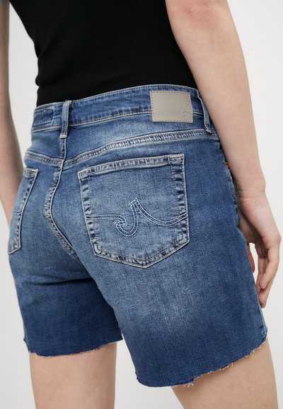 Vidutinio mėlynumo džinsinės šortai su paskutiniais apipjaustytais kraštais, galinėmis kišenėmis su siuvinėtais detalėmis ir mažyte pilka prekės ženklo etikete ant juosmens.
