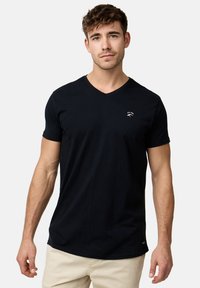 Camiseta de algodón negra con cuello en V, que presenta un pequeño logo blanco en el pecho, mangas cortas, corte relajado y textura suave.