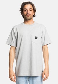 Grå bomulds T-shirt med korte ærmer og rund hals. Har en brystlomme med et sort logo-patch. Fitted, afslappet design.