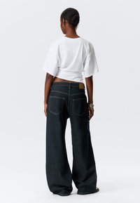 Wide-leg dark denim jeans with a high-rise waist and two back pockets, paired with a cropped white t-shirt. Smooth fabric texture.