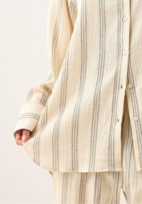 Lys beige button-up skjorte med lodrette sorte striber. Lavet af blødt, struktureret stof, med store manchetter og en afslappet pasform.