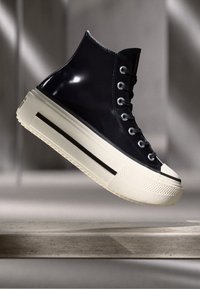 Højtop sneakers med en glansfuld sort overdel, hvid gummisul og sort stribe detalje. Har runde sølvøjer og en tekstureret tåhætte.