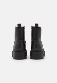 Svarta läderankelstövlar med en texturerad yta, fluffig krämfärgad foder upptill och en kraftig svart gummisula; har dragkedjestängning.