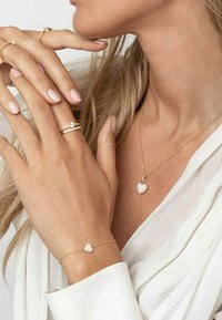 Set di gioielli in oro composto da una collana con pendente a forma di cuore e un braccialetto abbinato, decorati con accenti scintillanti e un design di catena delicato.