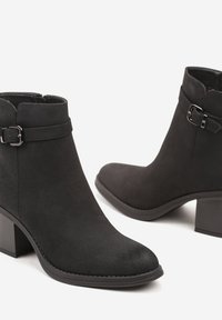 Bottines en suédine noire avec un petit talon carré, ornées d'une boucle sur le côté et d'une texture lisse. Design classique à bout arrondi.
