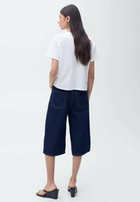 Hvid kortærmet top med huller, parret med mørkeblå brede denim culotter. Sorte blokhælsandaler fuldender outfittet.