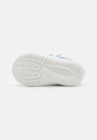 Suela de zapatilla deportiva blanca con patrón de agarre texturizado, con un acento en azul claro y rosa a lo largo del lateral, construcción flexible.