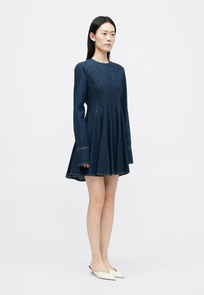 Tumši zili džinsa kleita ar garām piedurknēm, pieguļošu augšu un izplestu svārku. Iezīmē redzamas šuvju līnijas un apaļu izgriezumu.