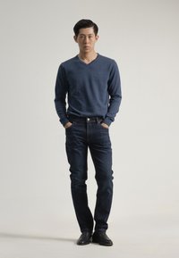 Suéter de punto azul marino con escote en V combinado con unos jeans de mezclilla oscuros. Suéter hecho de un tejido suave; los jeans tienen un corte clásico y no presentan desgastes visibles.